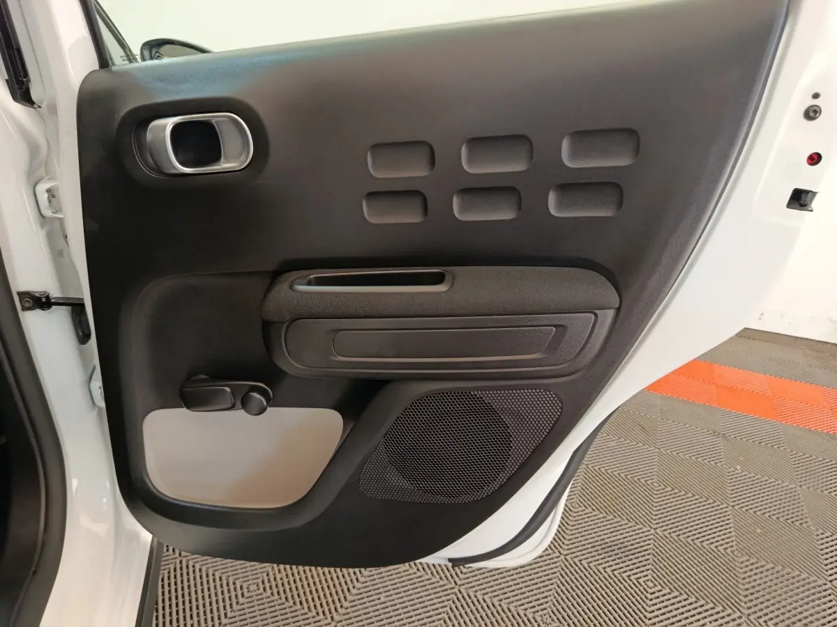 Vue rapprochée de la porte arrière gauche blanche d'une Citroën C3 2020 avec panneau intérieur noir et gris.