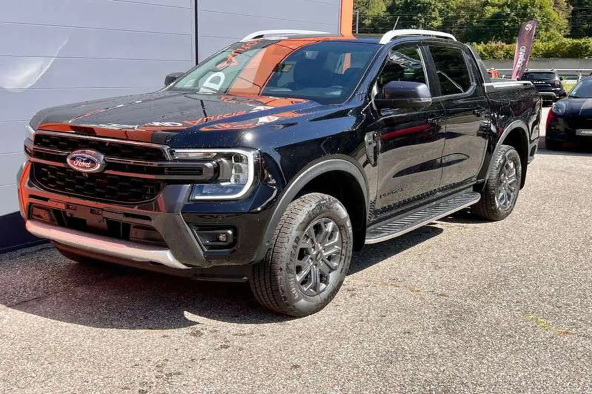 Ford Ranger 3.0 V6 Wildtrak Plus noir agate vu en 3/4 avant droit avec jantes alu et barres de toit visibles.