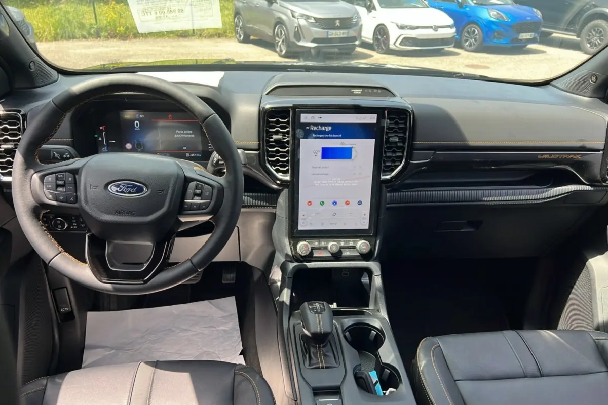 Vue intérieure avant du Ford Ranger Wildtrak Plus 2026, tableau de bord noir avec écran tactile vertical et volant cuir multifonctions.