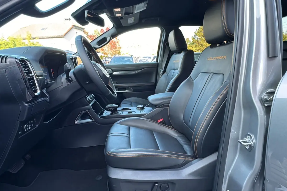 Intérieur avant côté conducteur du Ford Ranger gris iconic, sièges cuir noirs avec surpiqûres orange et logo Wildtrak brodé.