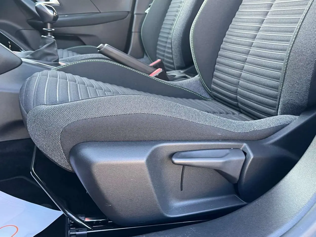Gros plan sur le siège avant droit du Peugeot 2008 2024, tissu noir avec surpiqûres vertes, levier de réglage manuel visible.
