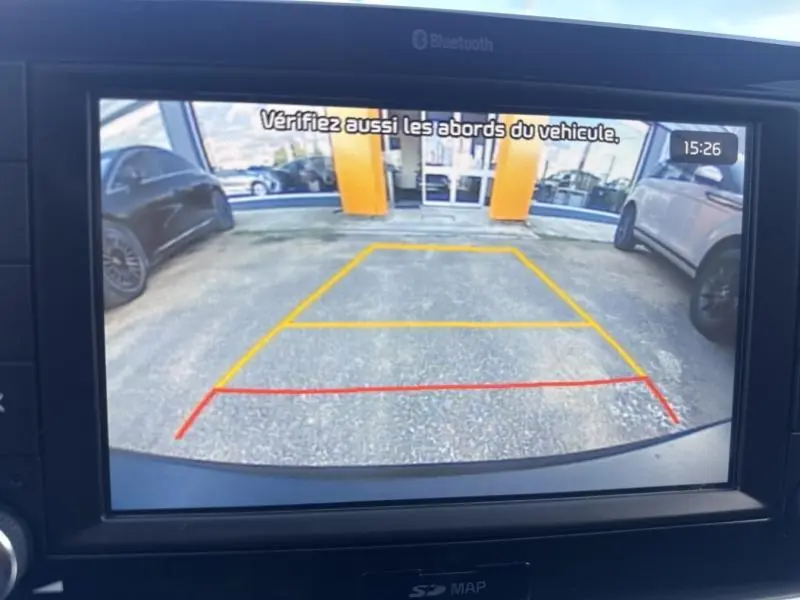 Vue écran caméra de recul d'une KIA STONIC 2019, montrant l'arrière avec lignes de guidage colorées et véhicules stationnés.