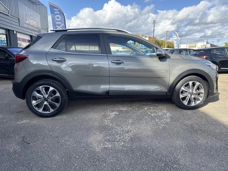 Profil droit du SUV KIA Stonic brun Sienne 2019 avec jantes alliage et barres de toit visibles en extérieur.