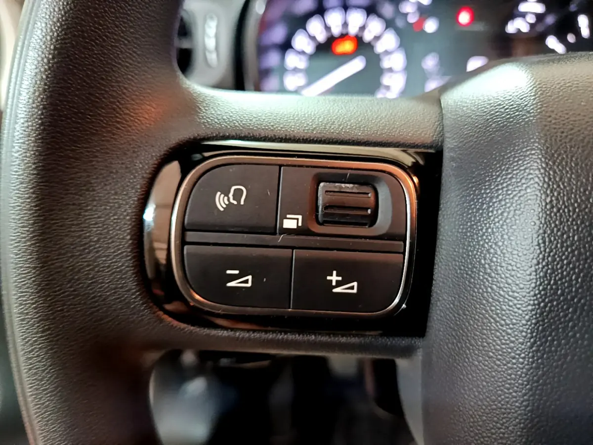 Gros plan sur les commandes vocales et de volume au volant d'une Citroën C3 beige, tableau de bord flou en arrière-plan.