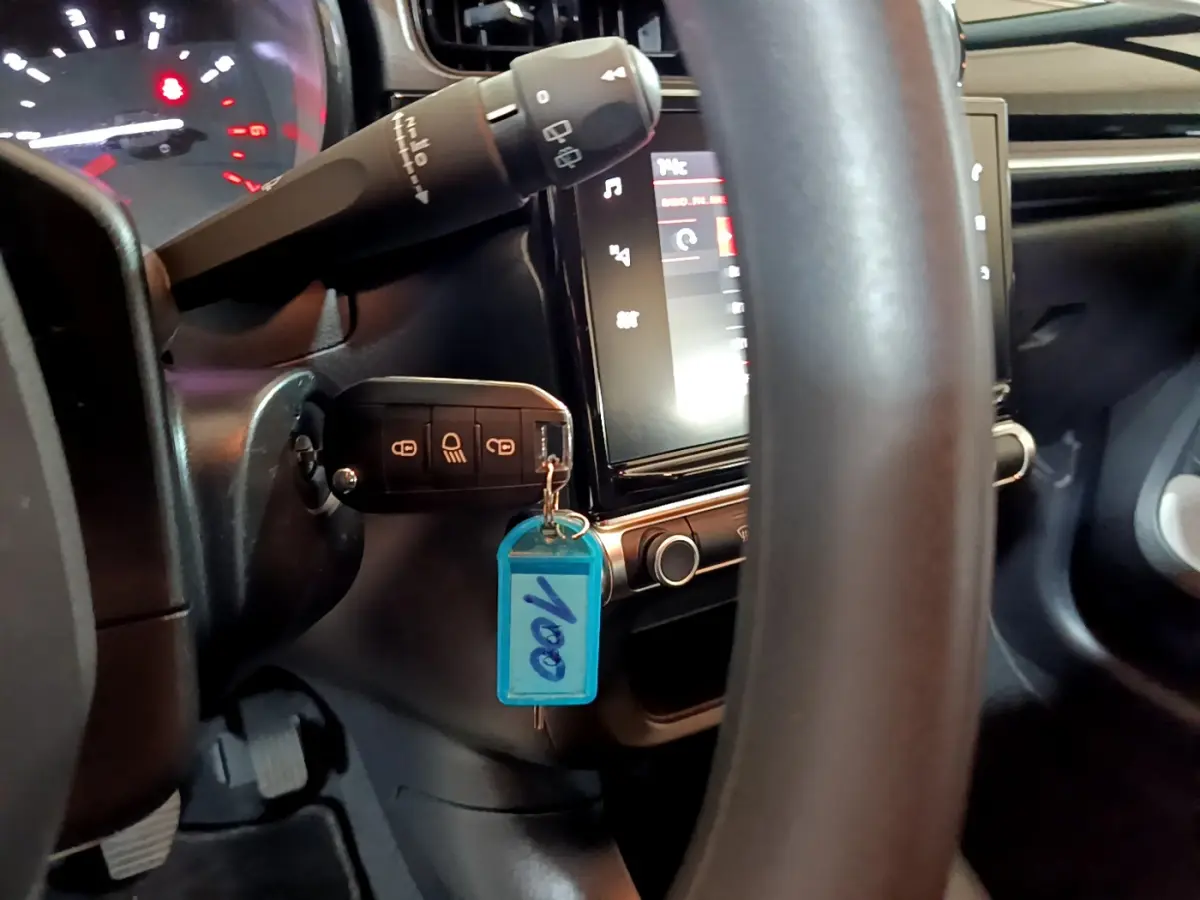 Vue rapprochée du tableau de bord et du volant noir d'une Citroën C3 beige avec clé insérée et écran tactile allumé.