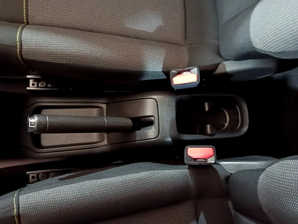 Vue plongeante sur la console centrale noire de la Citroën C3 avec frein à main manuel et deux ceintures rouges.