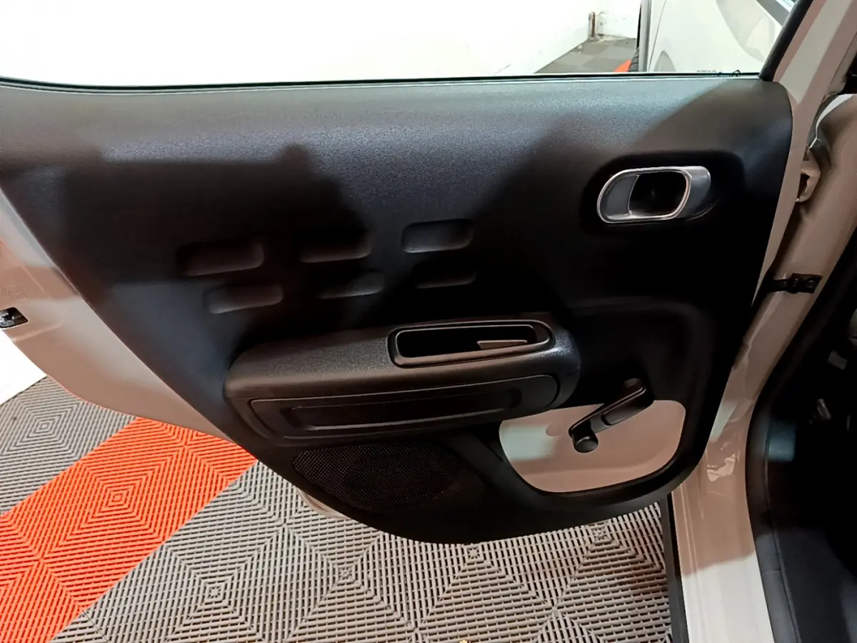 Vue rapprochée de la porte avant gauche beige de la Citroën C3 2022 avec poignée intérieure noire et manivelle de vitre.