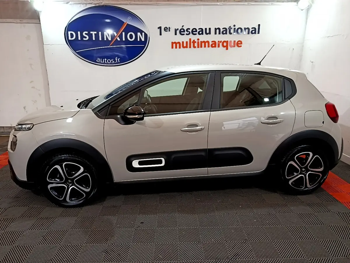 Profil côté gauche d'une Citroën C3 beige 2022 avec protections noires et jantes distinctives en intérieur showroom.