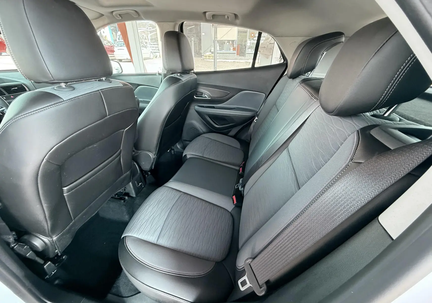 Vue intérieure arrière de l’Opel Mokka X 2016, sièges en cuir tissu gris noir avec ceintures de sécurité visibles.