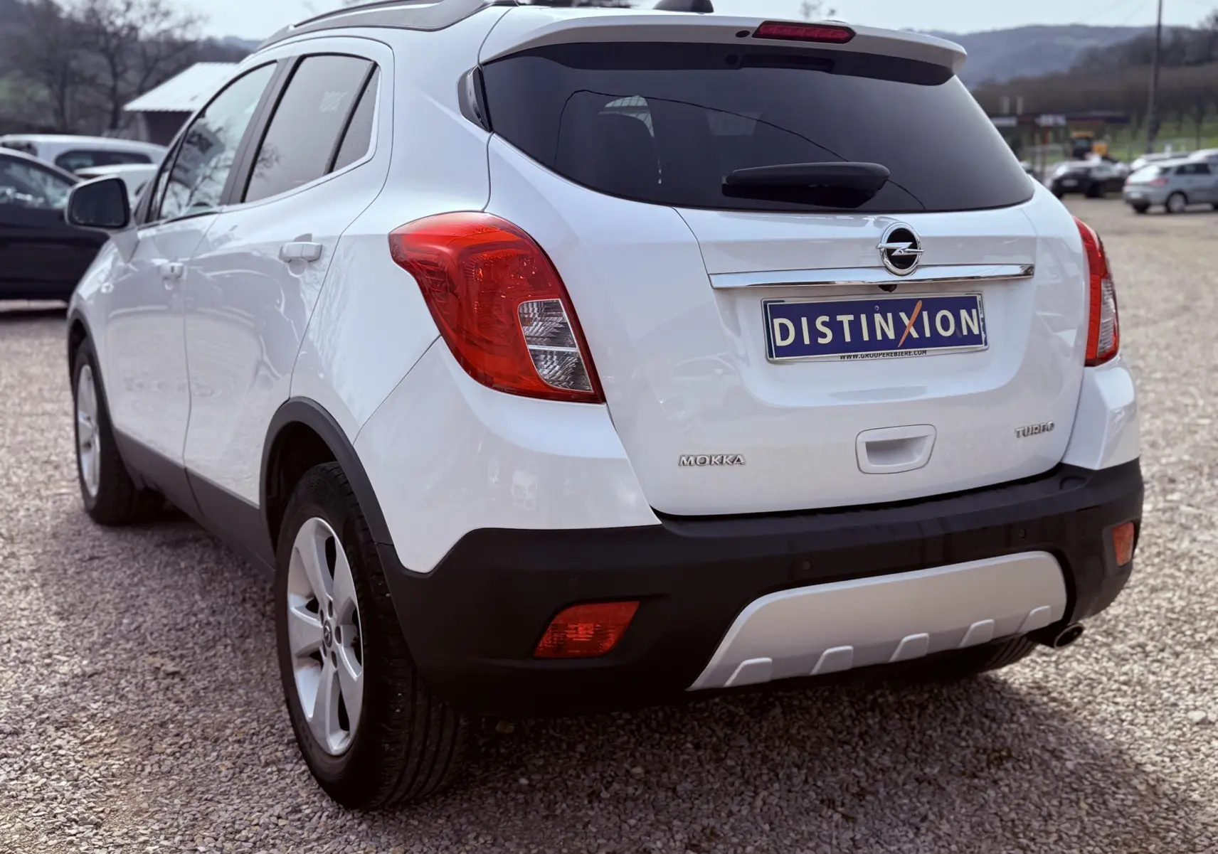 Vue 3/4 arrière gauche d’un Opel Mokka X blanc avec feux arrière rouges et plaque d’immatriculation Distinxion.