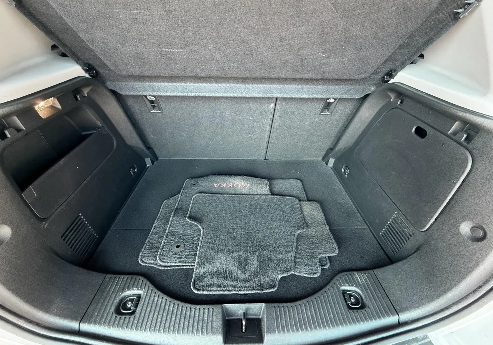 Vue ouverte du coffre arrière noir de l'Opel Mokka X blanc avec tapis de sol gris marqués MOKKA.