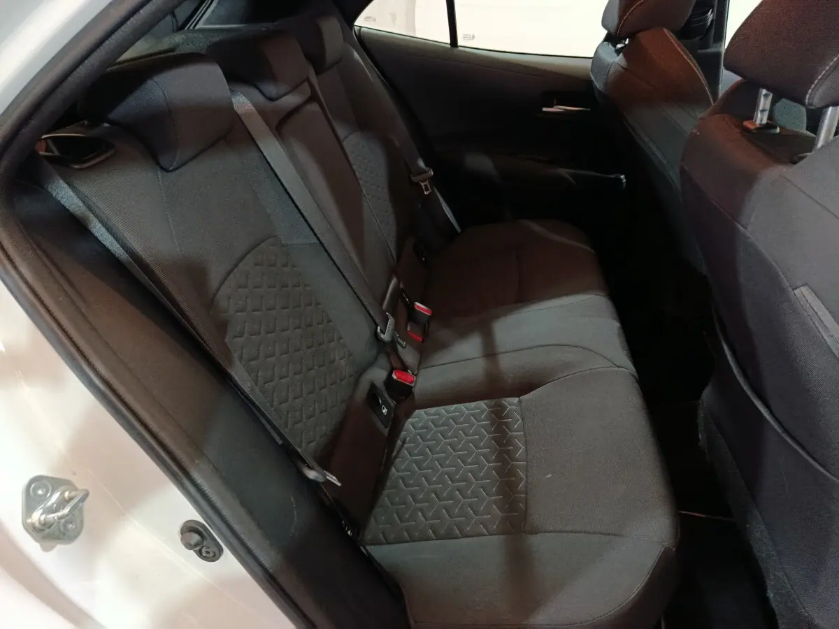 Vue intérieure côté gauche des sièges arrière noirs d'une Toyota Corolla Hybride 2022 blanche, porte ouverte.