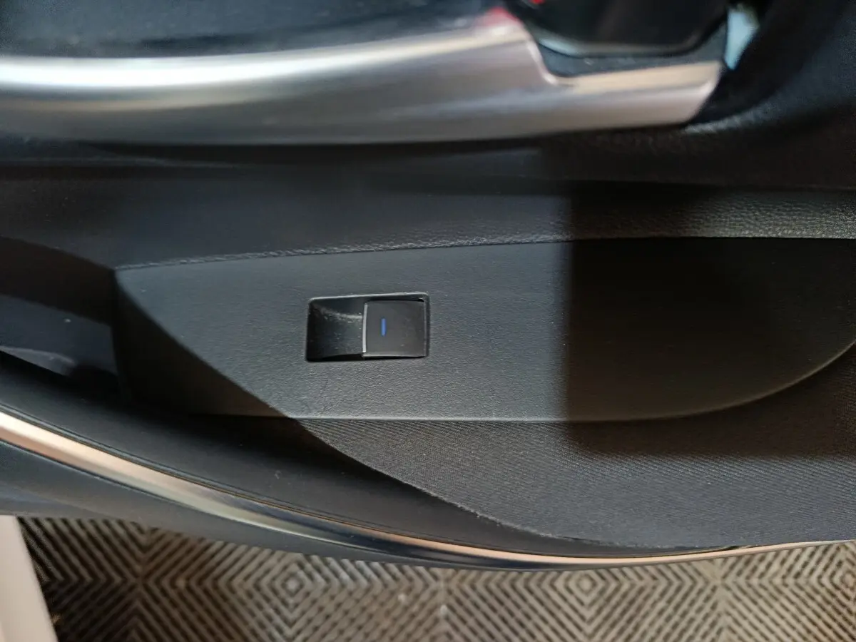 Gros plan sur le bouton de commande électrique de la portière intérieure d'une Toyota Corolla blanche, version hybride 2022.