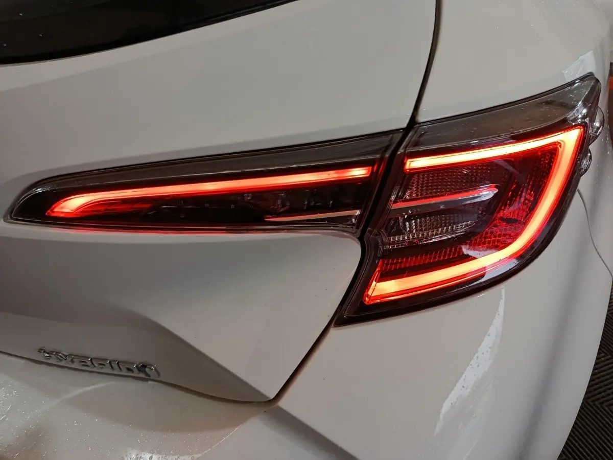 Gros plan sur le feu arrière droit allumé d'une Toyota Corolla hybride blanche, soulignant ses lignes LED distinctives.