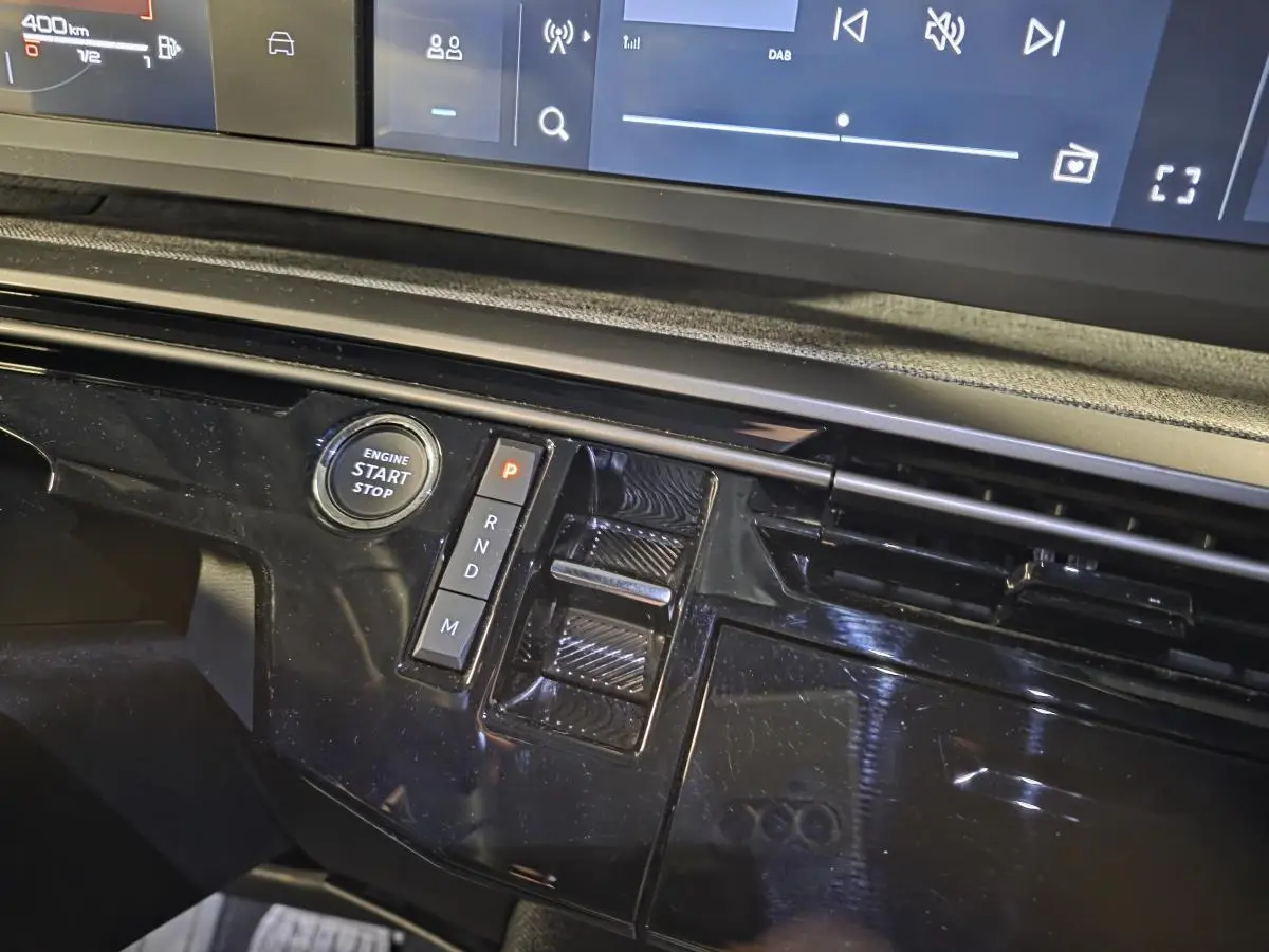 Gros plan sur la console centrale noire laquée du Peugeot 5008 2025 avec boutons de boîte auto et bouton start/stop.