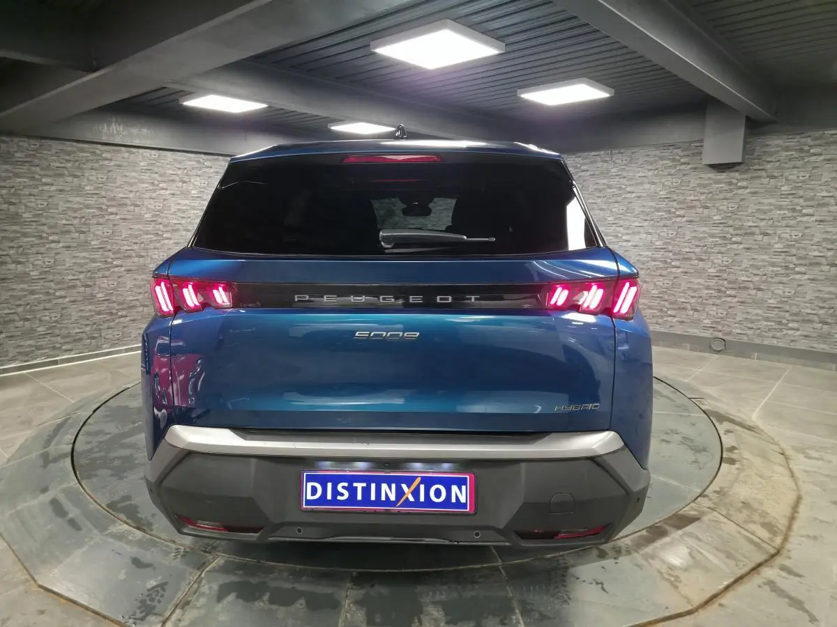 Vue arrière d'un Peugeot 5008 bleu métallisé 2025 avec feux arrière LED à trois griffes et bandeau noir laqué.