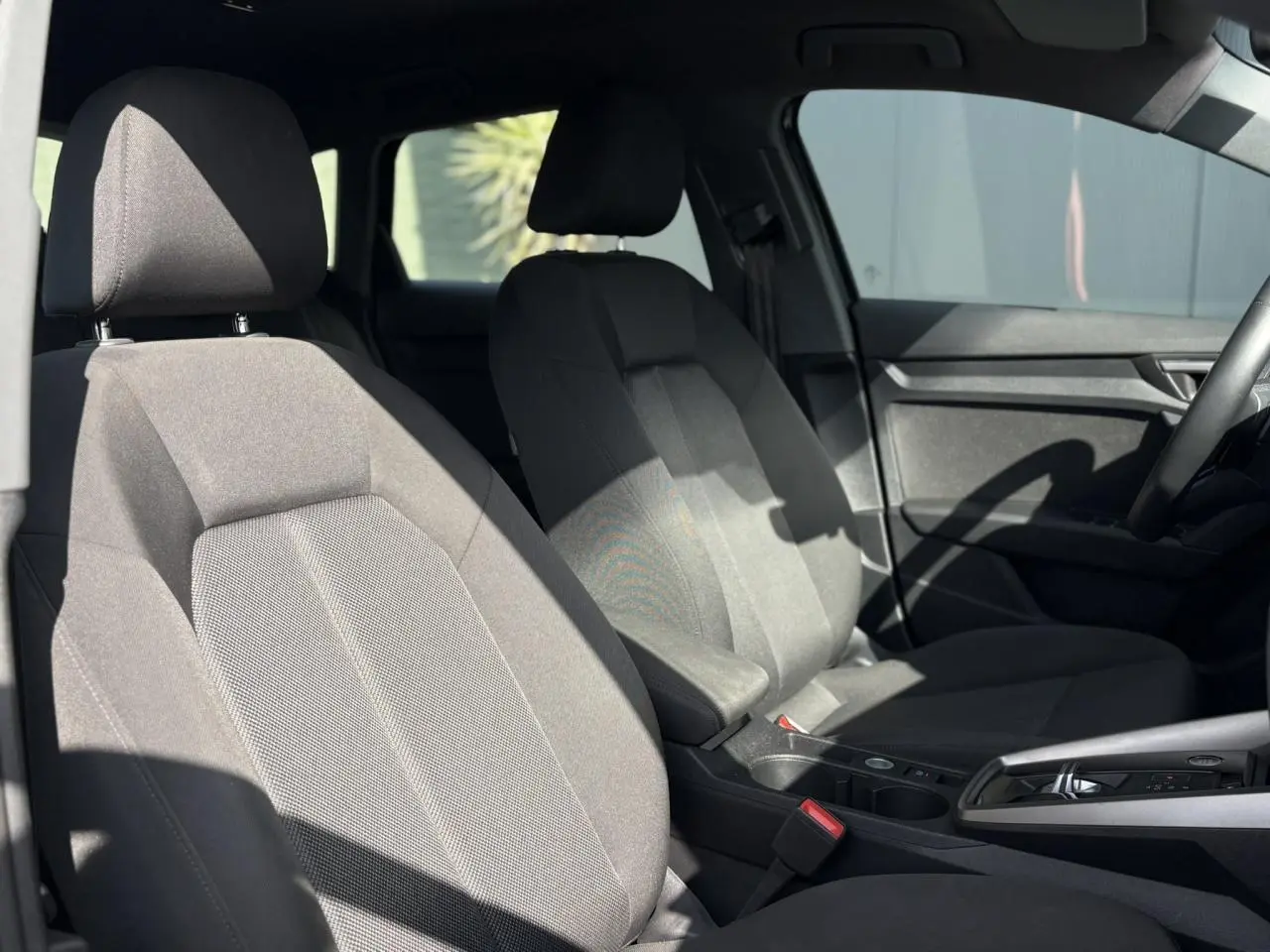 Vue intérieure sur les sièges avant en tissu gris de l'Audi A3 Sportback 30 TFSI 2023 avec accoudoir central réglable.