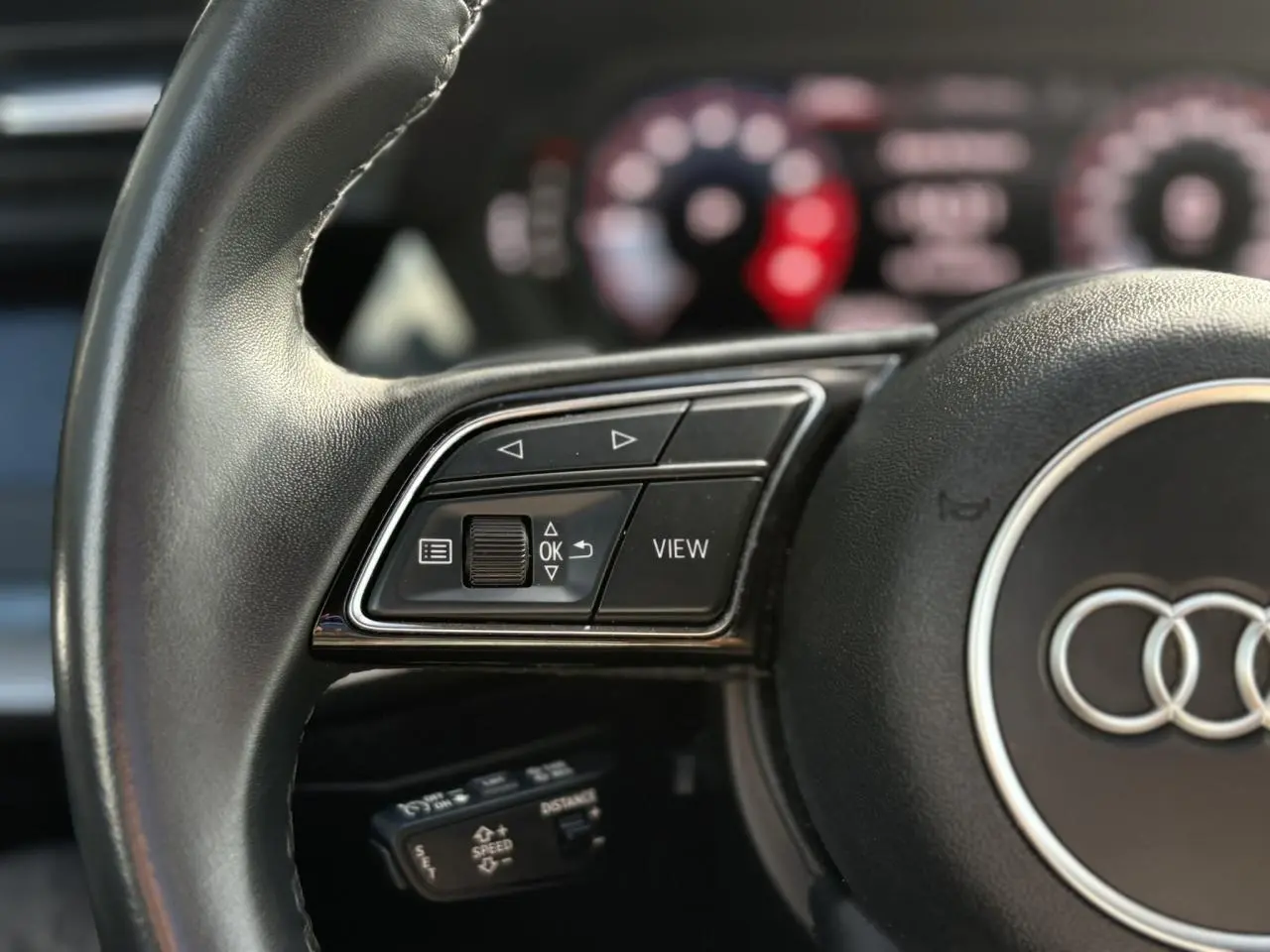 Gros plan sur le volant noir de l'Audi A3 Sportback 30 TFSI 2023 avec commandes multifonctions et affichage numérique flou.