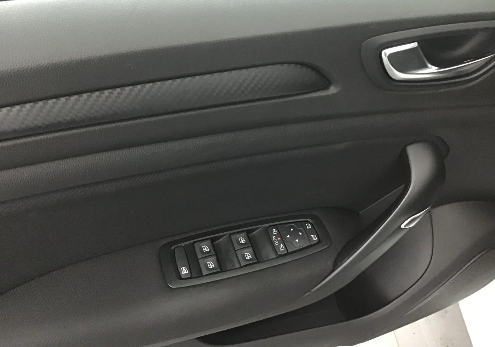 Panneau de porte côté gauche noir de la Renault Mégane IV Berline blanche, avec commandes électriques des vitres et poignée intégrée.