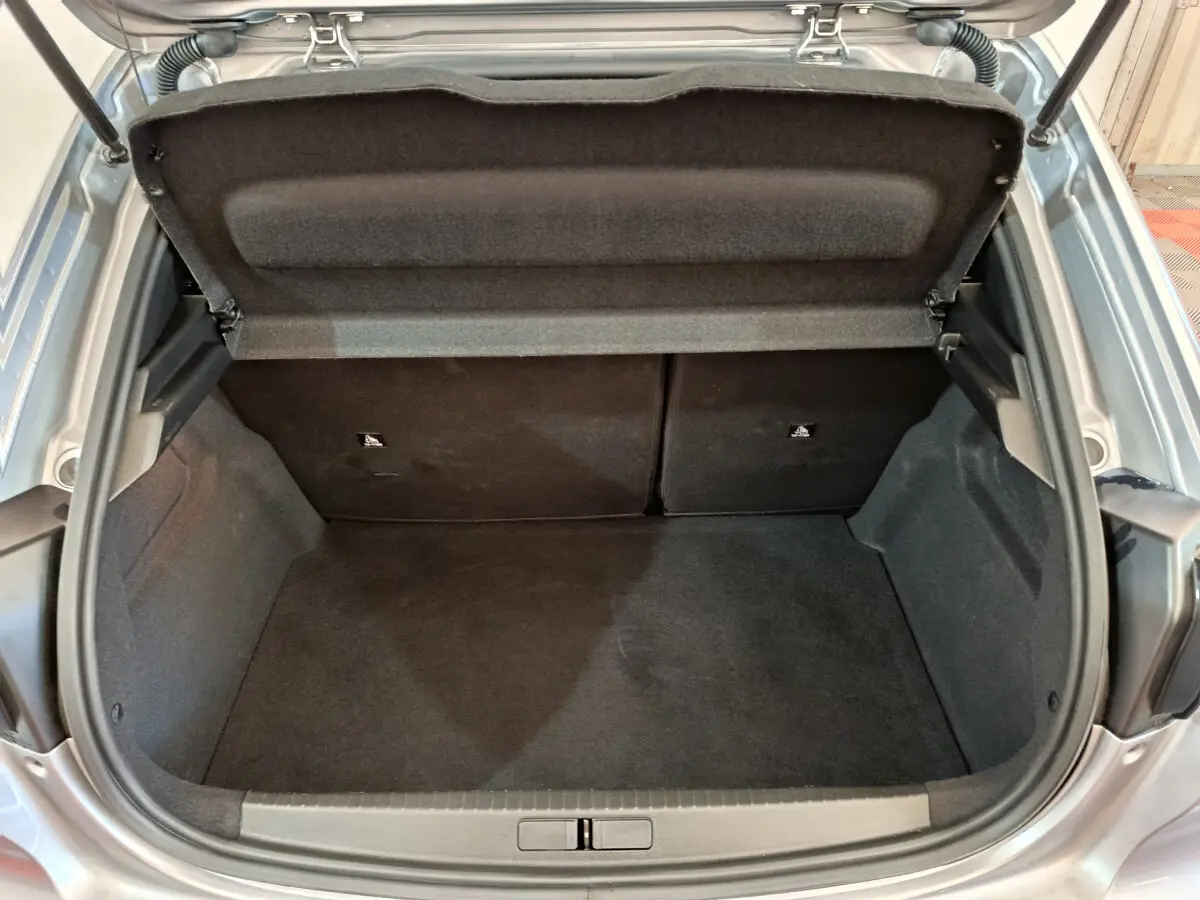 Coffre ouvert vu de l'arrière d'une Peugeot 208 gris clair, montrant l'espace de rangement et la tablette arrière.