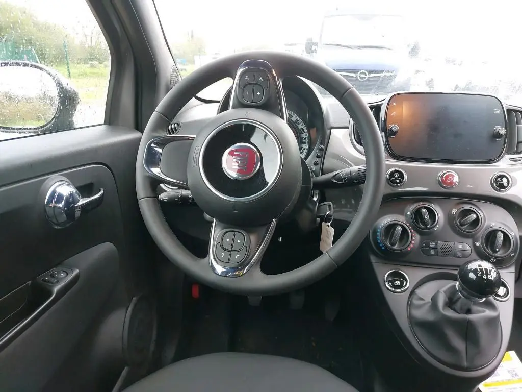 Vue intérieure centrée sur le volant et la console d'une Fiat 500 2023, avec boîte manuelle et tableau de bord gris Electroclash.