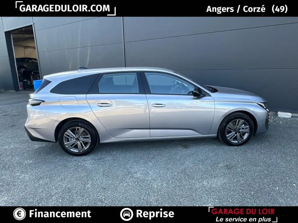 Profil côté droit d'une Peugeot 308 break gris clair 2023 stationnée devant un mur gris, roues alliage visibles.