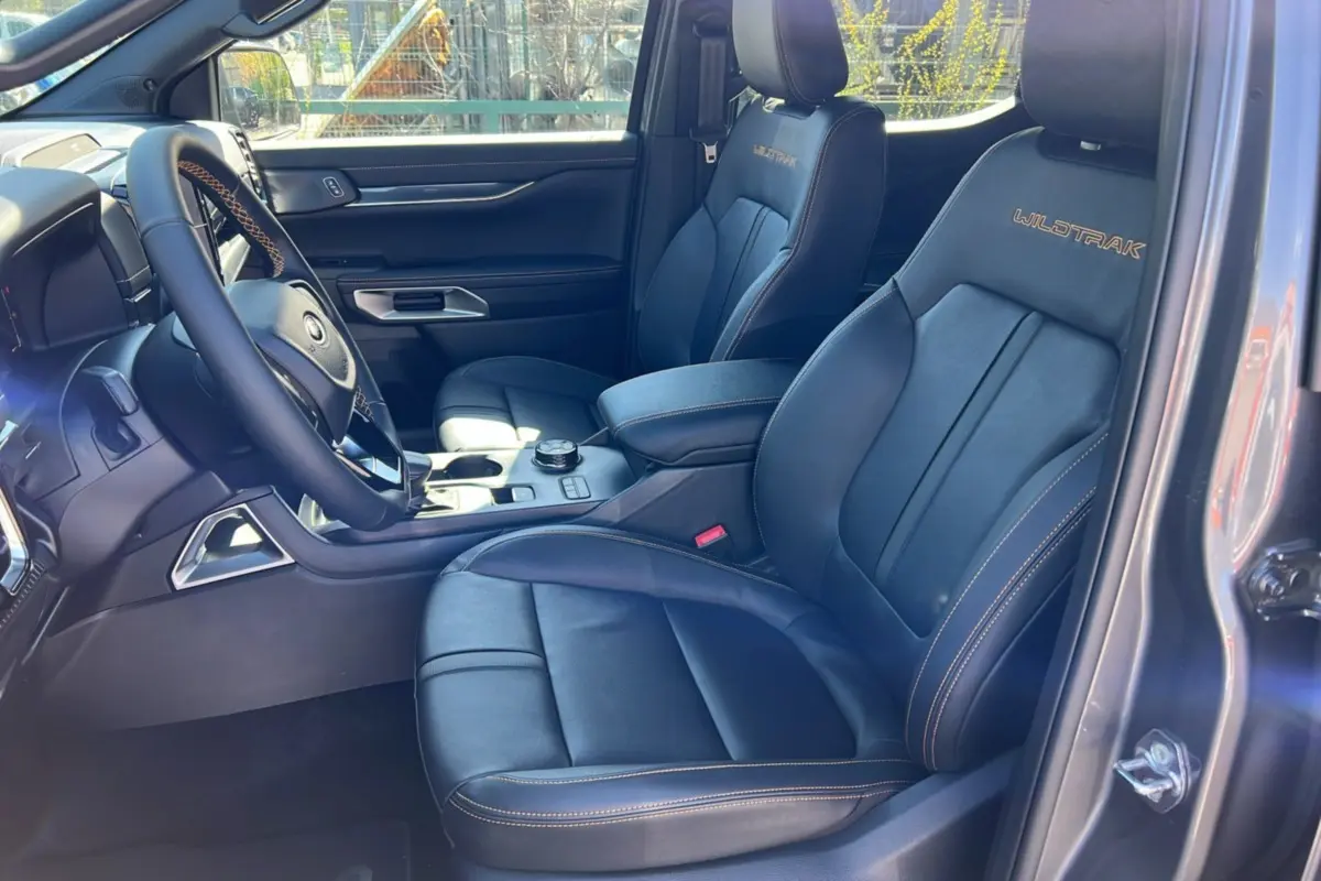 Vue intérieure côté conducteur du Ford Ranger 2025 gris carbone, sièges cuir noirs avec logo Wildtrak brodé.