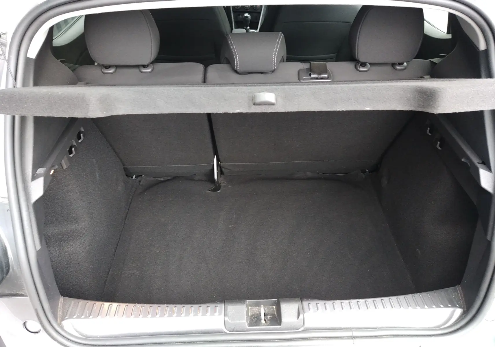 Coffre ouvert vu de l'arrière d'une Dacia Sandero gris 2024, montrant l'espace de chargement et la banquette arrière.