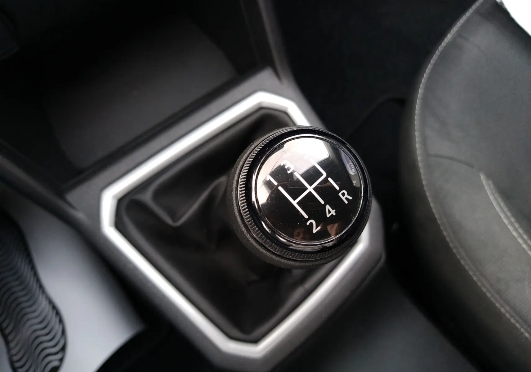 Gros plan sur le levier de vitesses manuel noir de la Dacia Sandero 2024, entouré d’un cadre argenté, avec siège tissu gris visible.