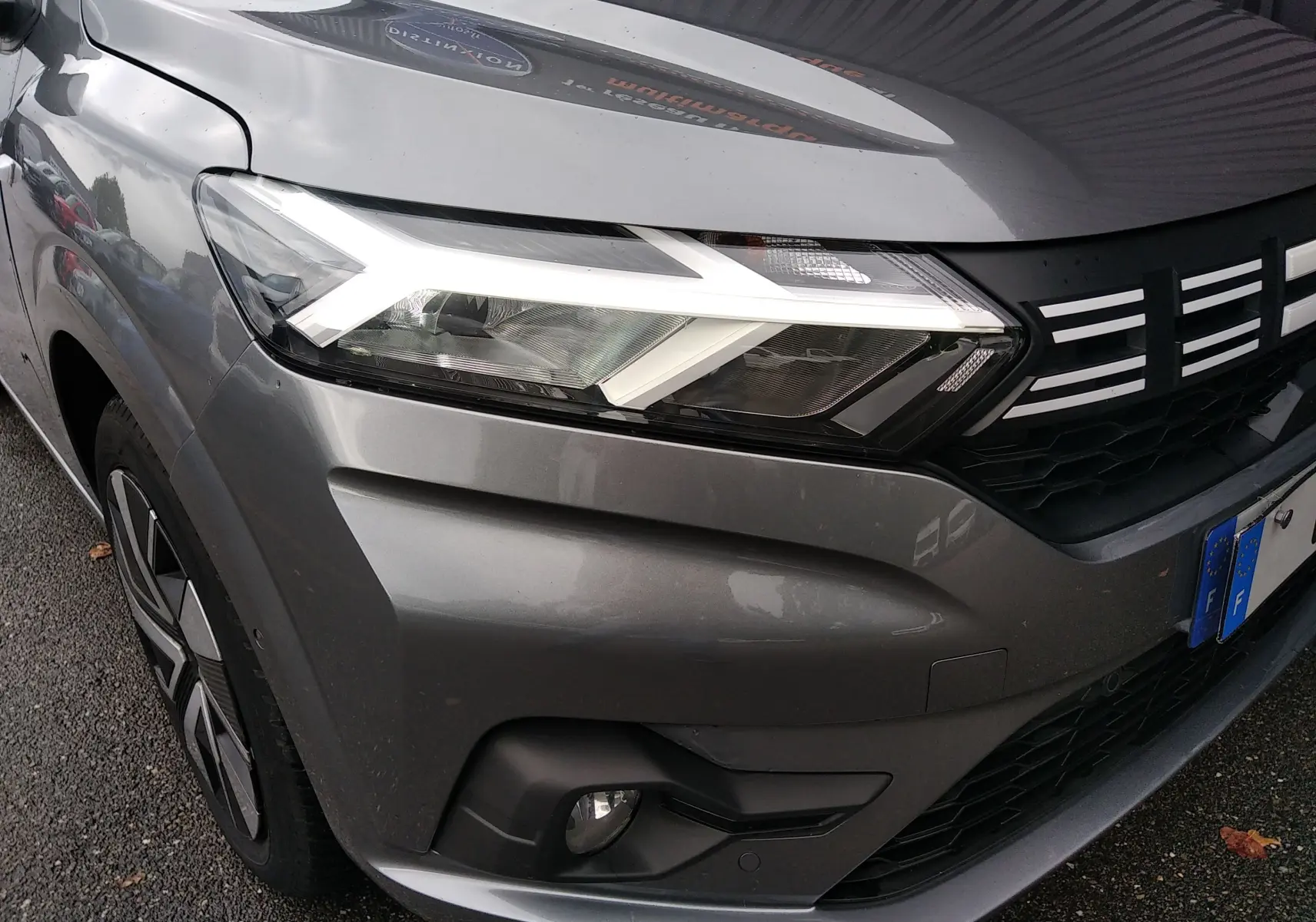 Gros plan sur l'avant droit gris d'une Dacia Sandero 2024, mettant en valeur le phare LED et la calandre noire.