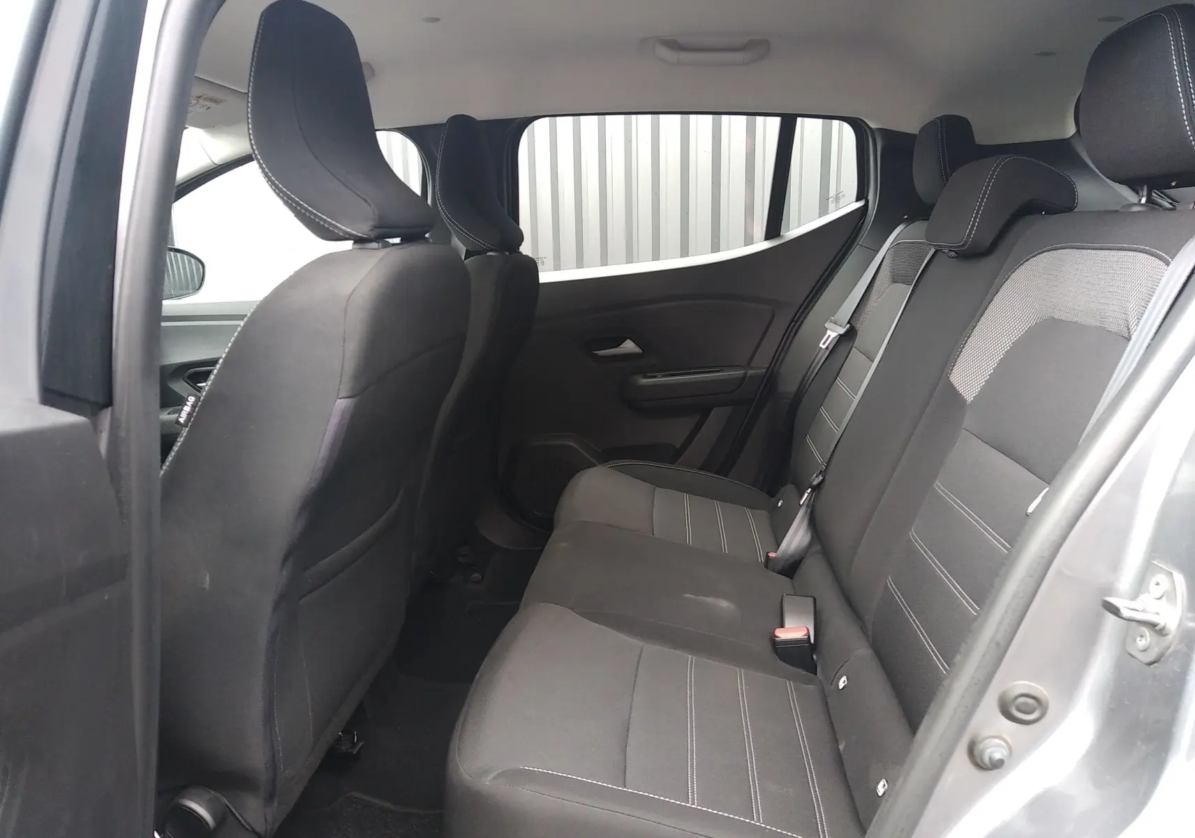 Vue intérieure côté droit des sièges arrière en tissu gris foncé de la Dacia Sandero 2024, porte ouverte.