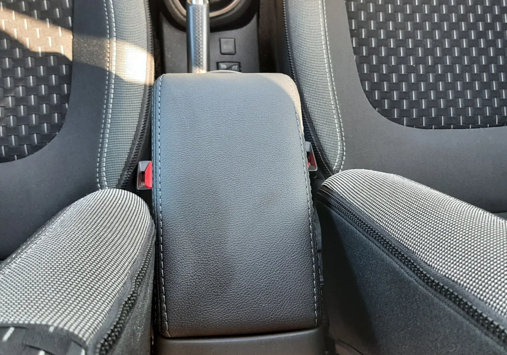 Vue plongeante sur l'accoudoir central noir et les sièges en tissu gris du Renault Captur 2018 essence.