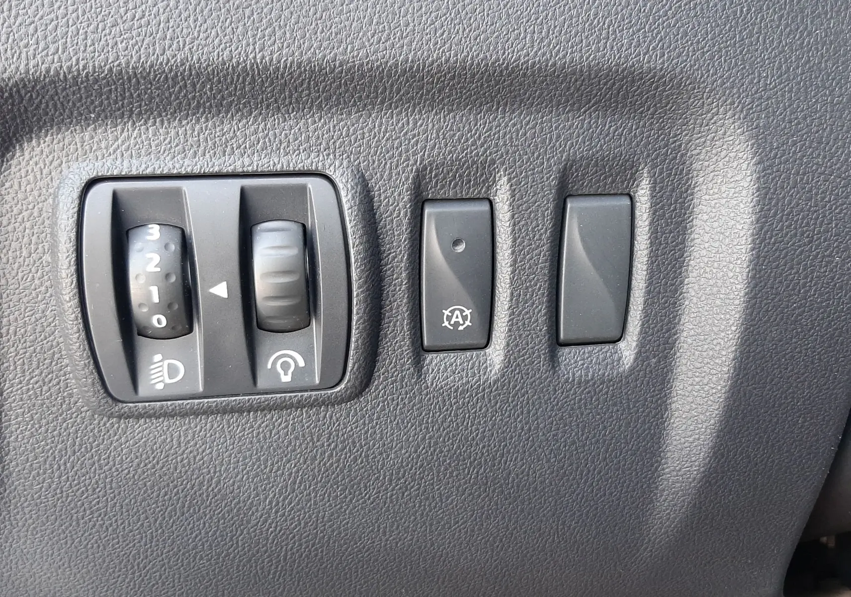 Gros plan sur les commandes de réglage des phares et du système start-stop du Renault Captur 2018, intérieur noir.