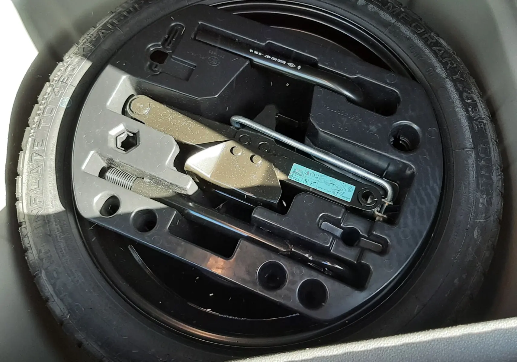 Gros plan sur la roue de secours noire et son kit d'outils intégré dans le coffre d'un Renault Captur gris cassiope toit noir.