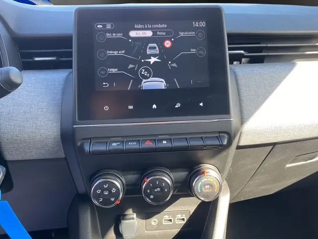 Tableau de bord de Renault Clio V gris Rafale, affichant l'écran tactile du système d'aides à la conduite et commandes manuelles de climatisation.