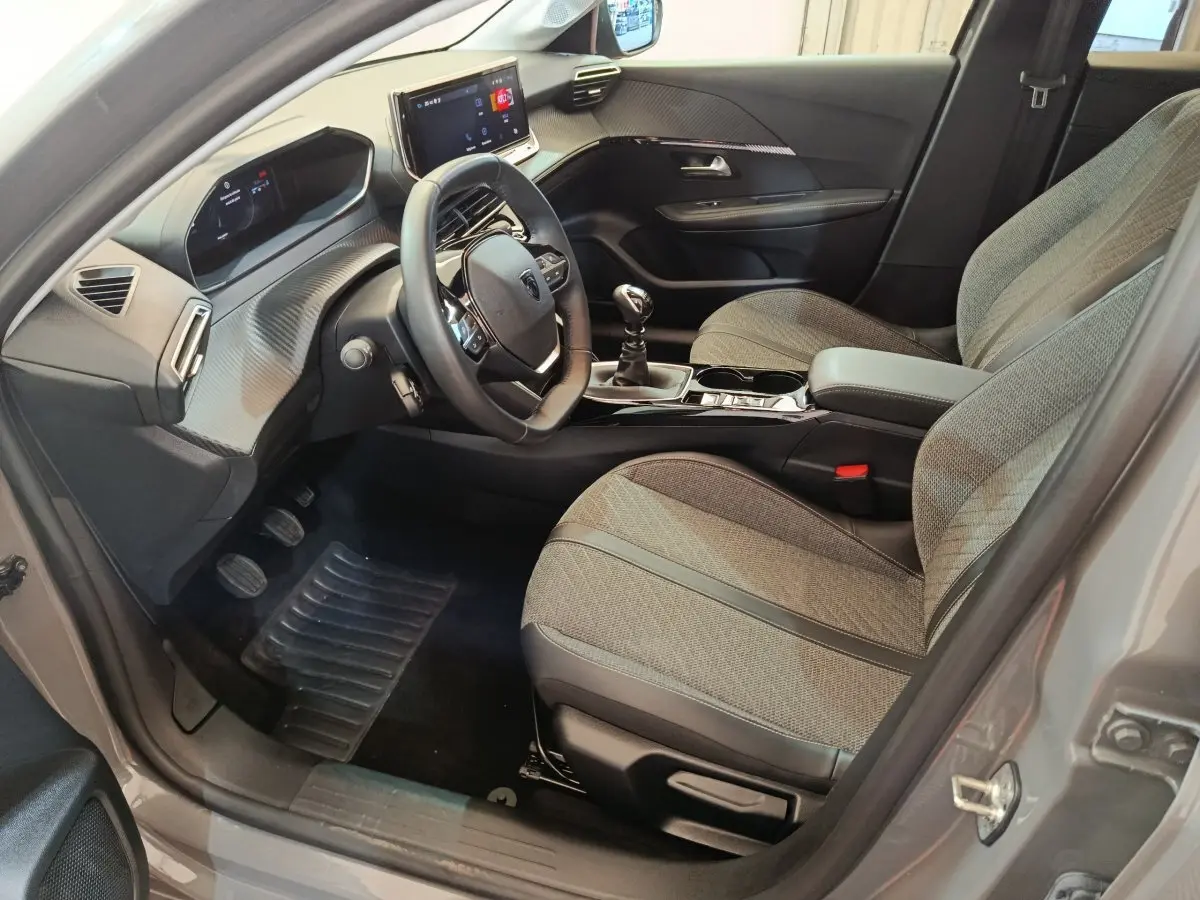 Intérieur avant droit de la Peugeot 208 PureTech 100 S&S Allure 2025 gris foncé avec tableau de bord numérique et volant cuir.