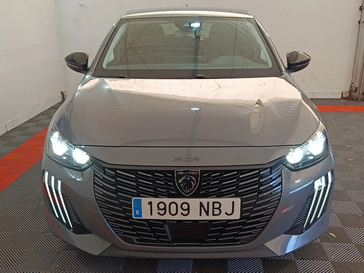 Vue frontale d'une Peugeot 208 gris foncé avec phares LED allumés et calandre noire distinctive.