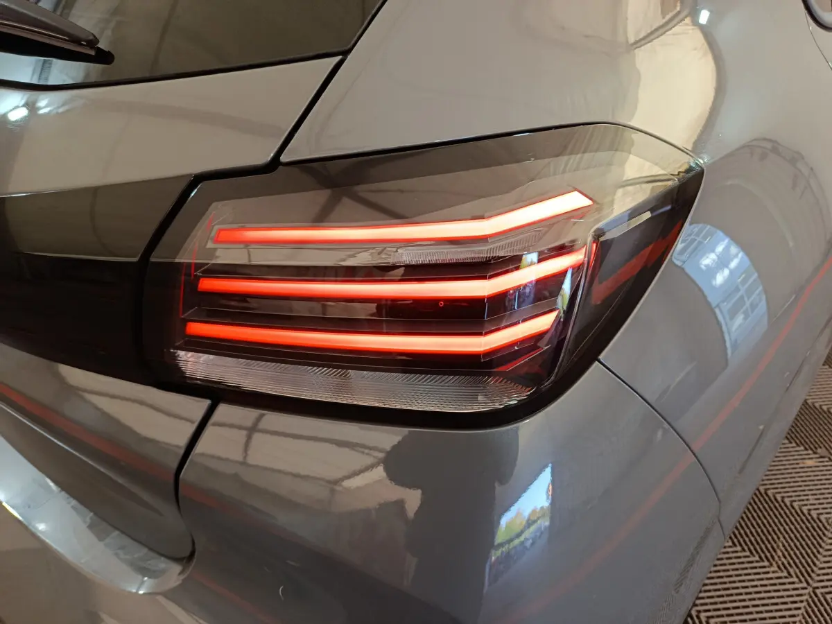 Feu arrière droit allumé sur Peugeot 208 gris foncé, vue rapprochée du coin arrière du véhicule.