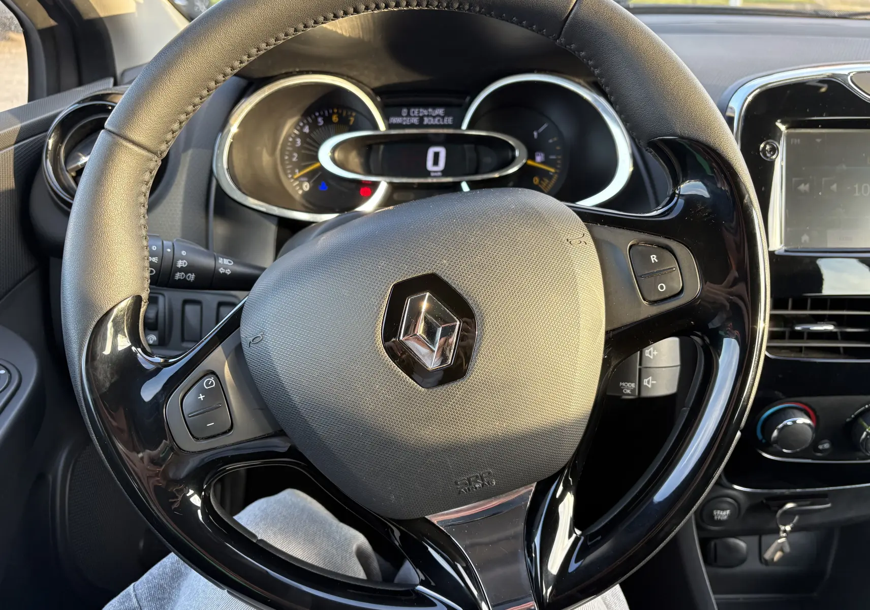 Vue rapprochée du volant noir et gris de la Renault Clio IV 2013 avec tableau de bord et écran GPS en arrière-plan.