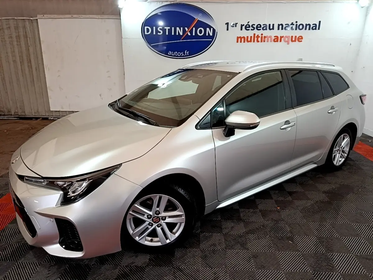 Suzuki Swace gris clair vue 3/4 avant droit en intérieur avec jantes alliage et vitres teintées.