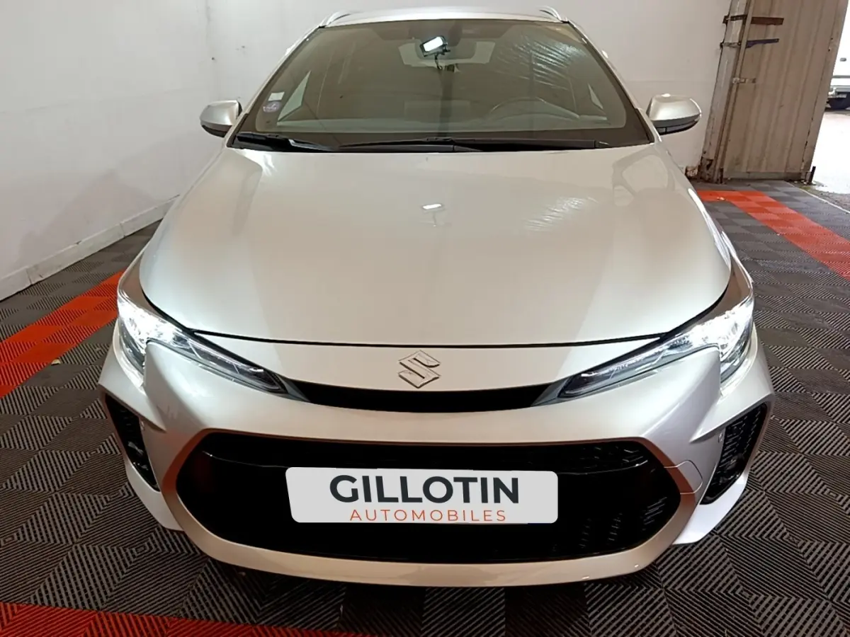 Vue avant rapprochée d'une Suzuki Swace 1.8 Hybrid Privilege gris clair avec calandre noire et phares LED allumés.