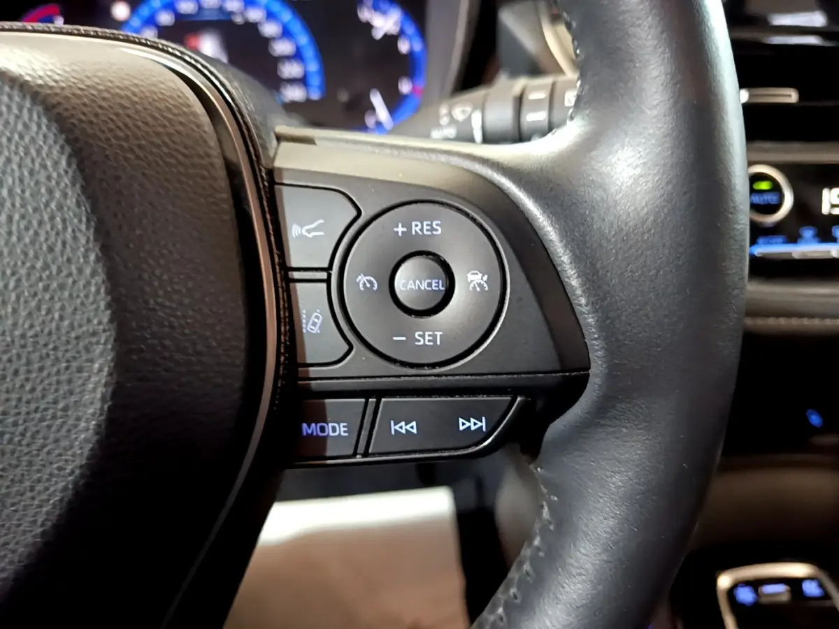 Gros plan sur le volant cuir et alu multifonctions noir du Suzuki Swace gris clair, avec commandes de régulateur et audio.