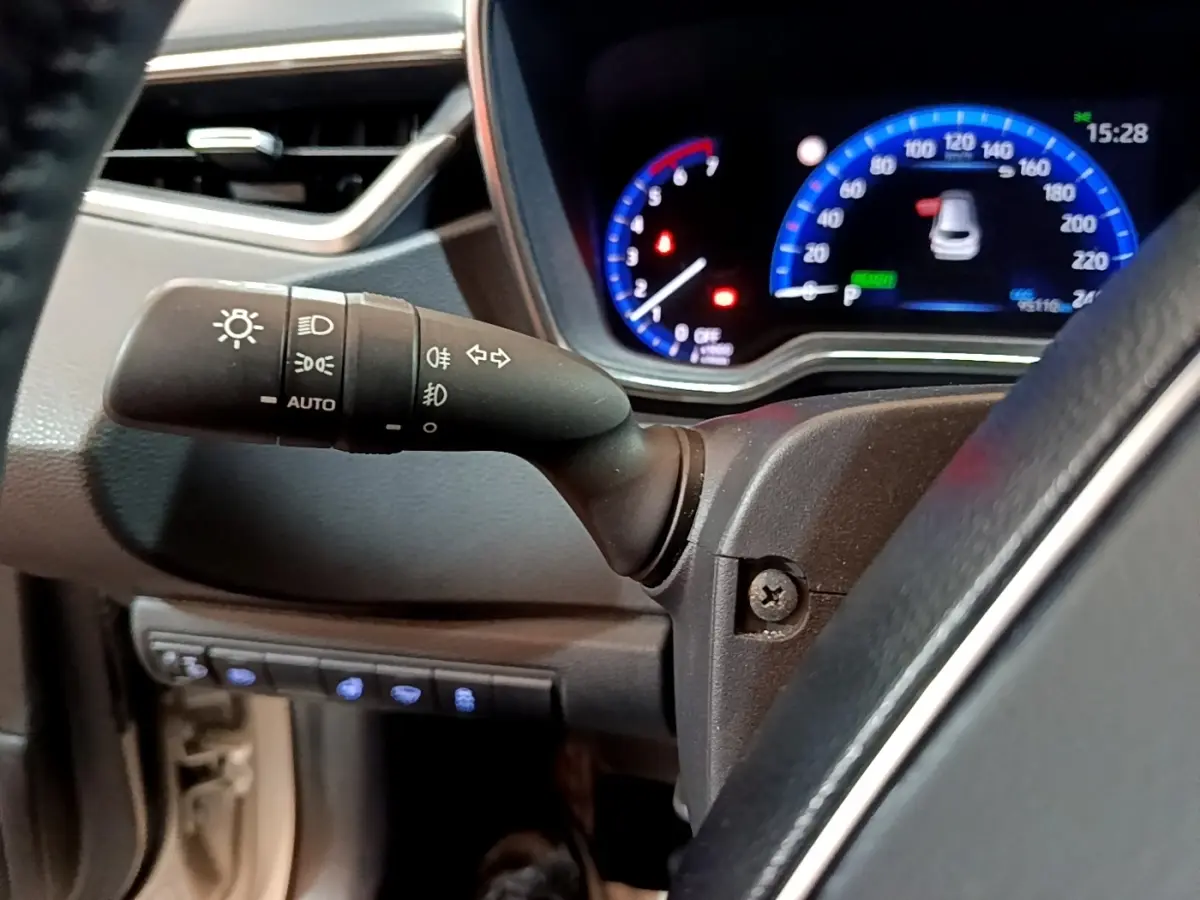 Gros plan sur la manette de commande des phares et clignotants à gauche du volant dans l’habitacle du Suzuki Swace gris clair.