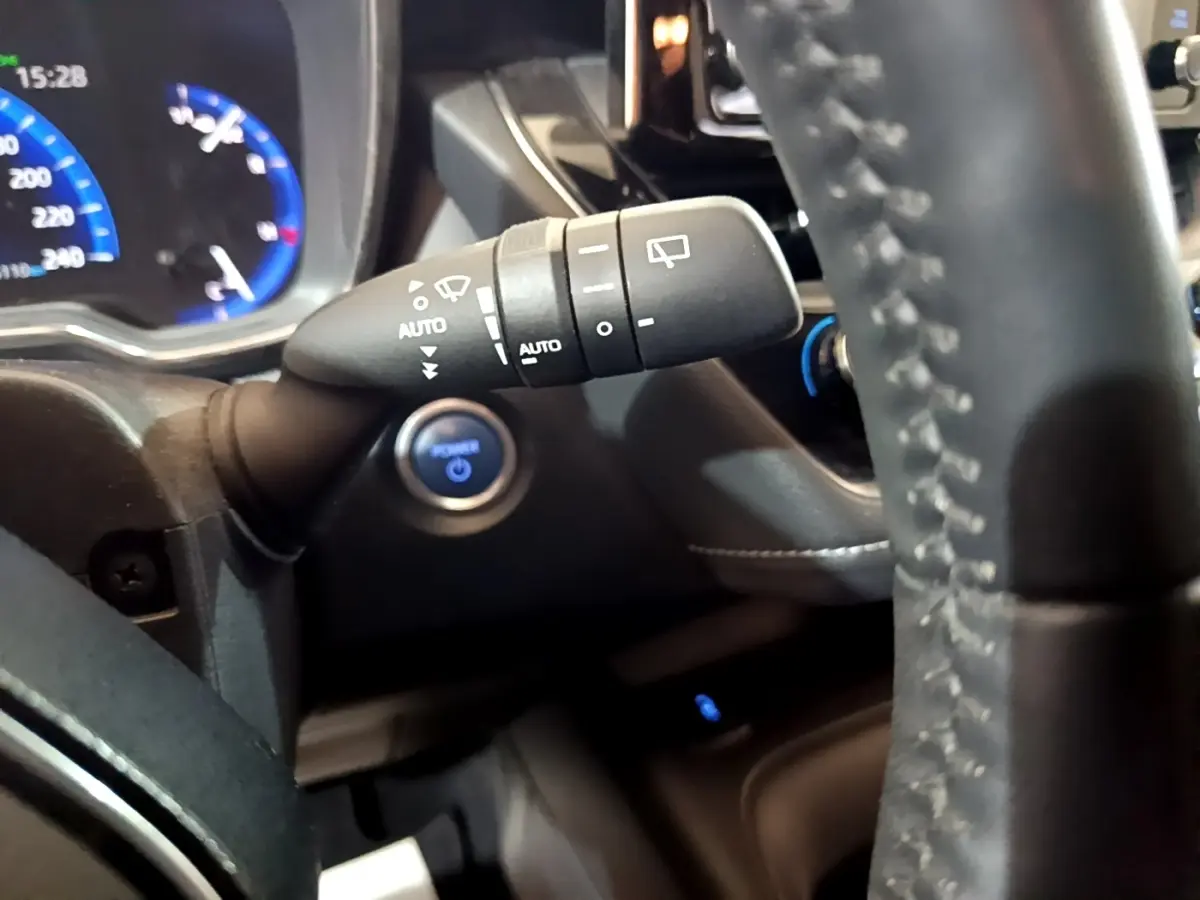 Gros plan intérieur sur la manette d’essuie-glace et le volant cuir du Suzuki Swace gris clair, avec tableau de bord digital bleu.