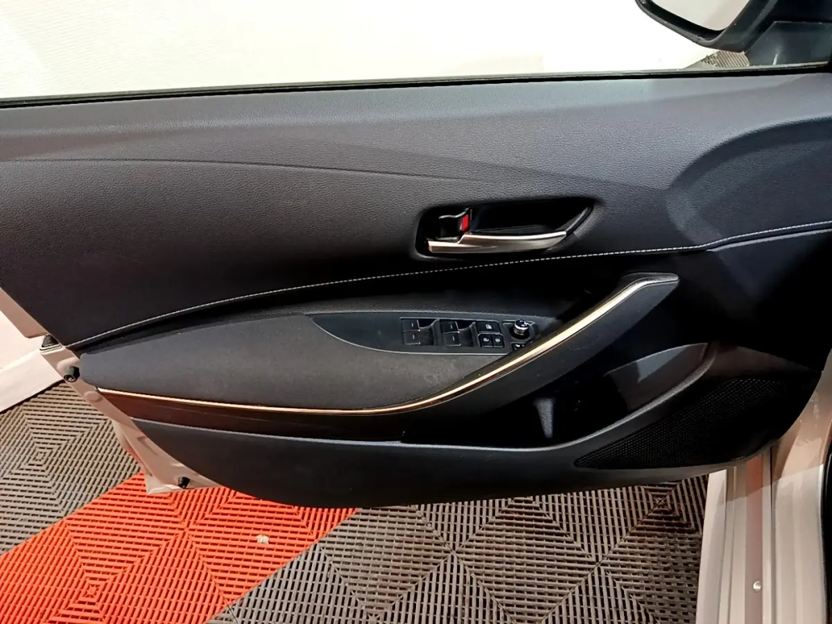 Vue intérieure côté gauche de la porte avant grise claire du Suzuki Swace 1.8 Hybrid Privilege avec poignée alu et commandes vitres.