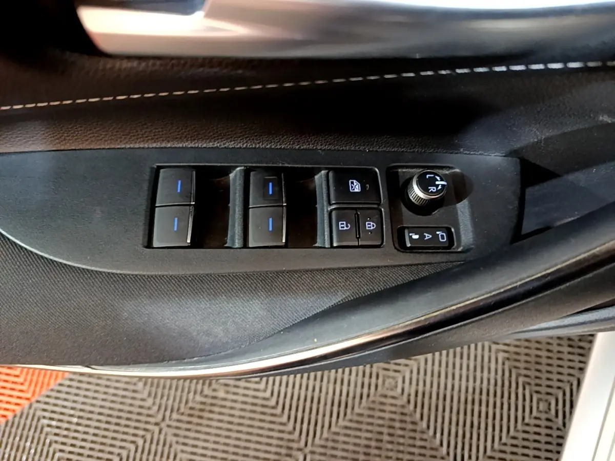 Vue rapprochée des commandes de lève-vitres et réglage des rétroviseurs sur la porte côté conducteur d'une Suzuki Swace gris clair.