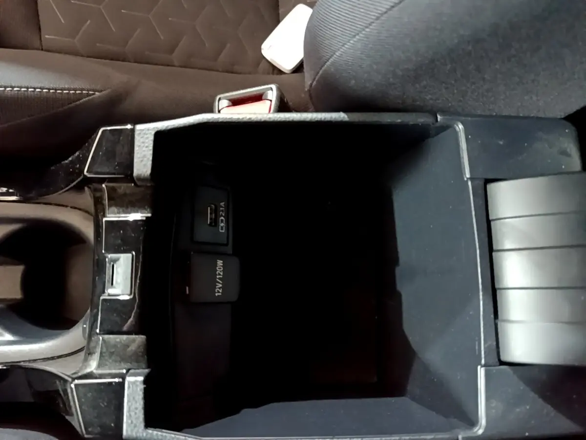 Vue plongeante sur la console centrale noire du Suzuki Swace 1.8 Hybrid Privilege avec prise USB et 12V visible.