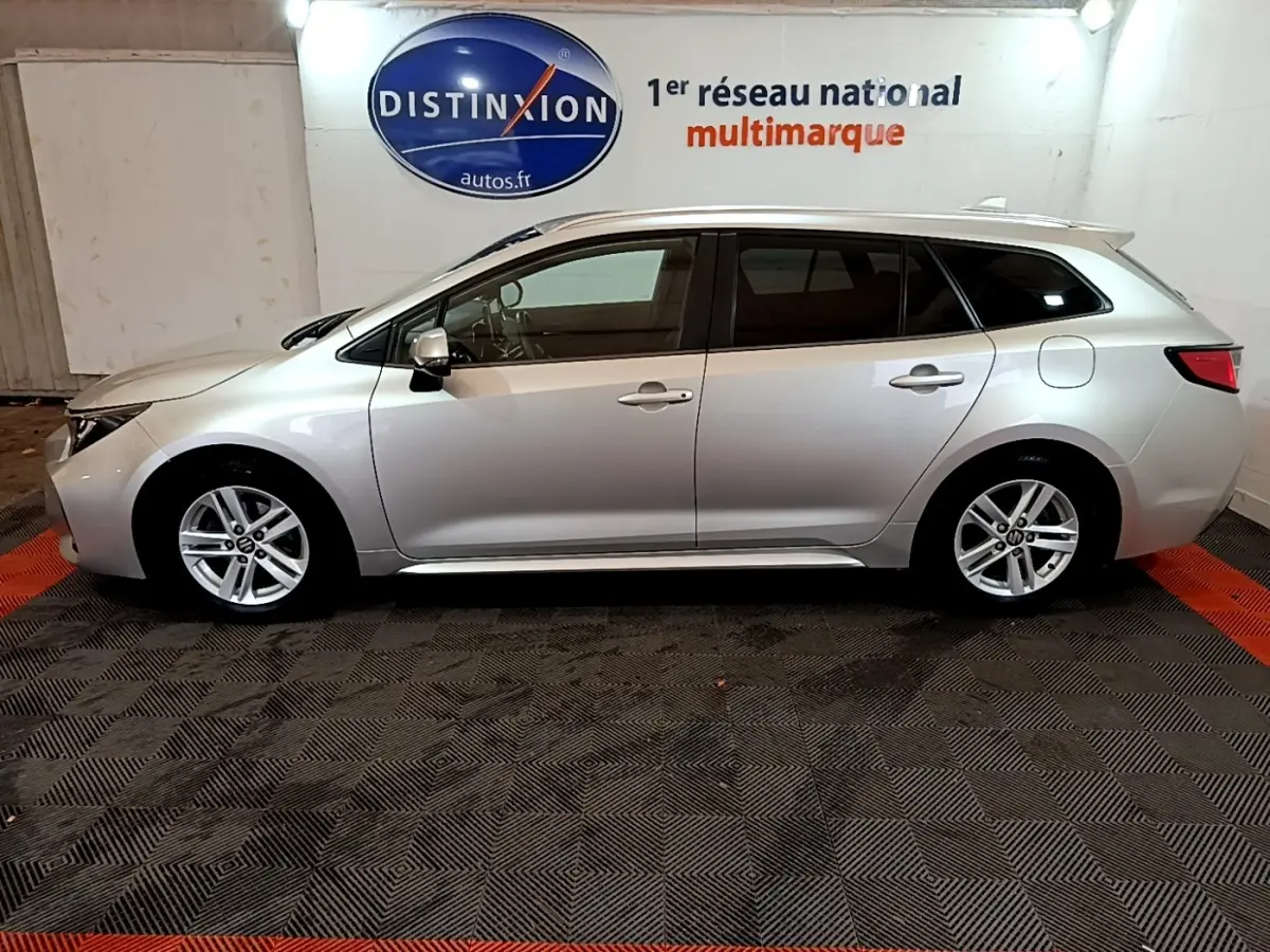 Profil droit d'une Suzuki Swace gris clair 2021 en version hybride, avec jantes alliage et toit chromé visible en intérieur showroom.