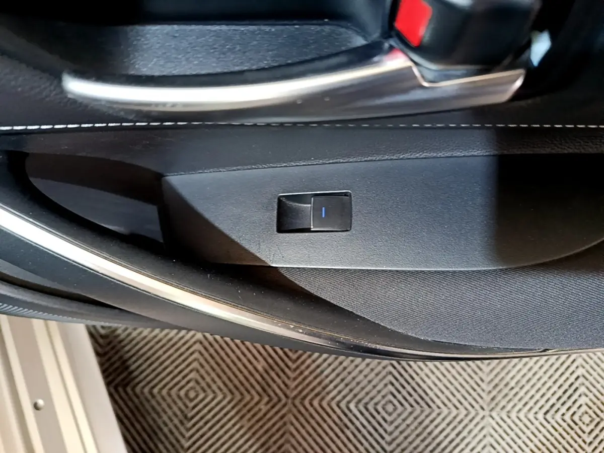 Détail de l'intérieur côté porte avant avec bouton de verrouillage, garniture noire et surpiqûres blanches.