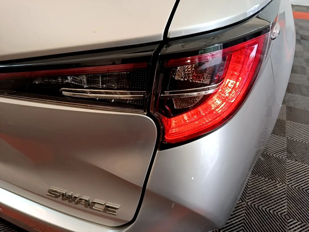 Gros plan sur le feu arrière droit d'une Suzuki Swace gris clair, mettant en valeur le logo et la finition lisse du coffre.